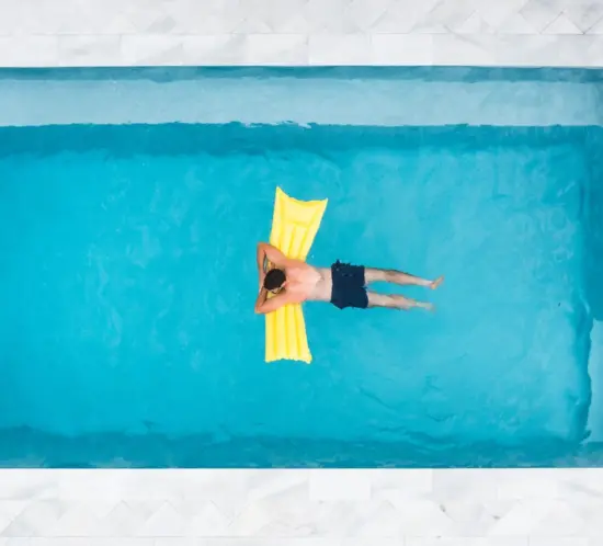Man relaxing, swimming in the swimming pool in his own backyard.